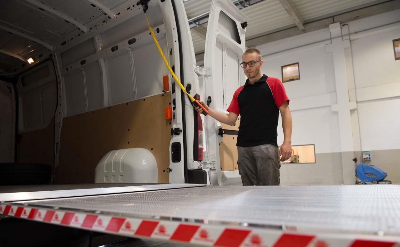 Technicien installant un hayon élévateur à l'arrière d'un fourgon en atelier